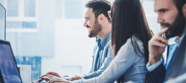 three coworkers at desk in office conversing and looking at computer together